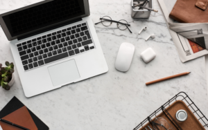 A desk with a laptop, mouse, glasses, and writing utensils