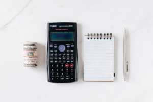 A table with a calculator, roll of bills, pen, and notebook