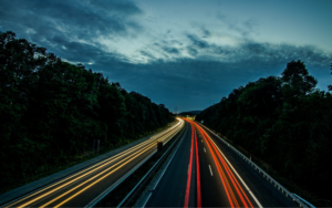 A road at dusk with trees on either side, showing car lines along the path