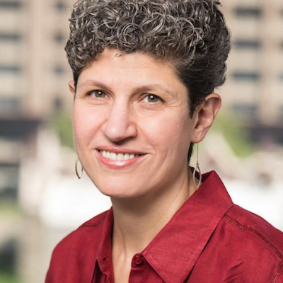 A woman with short curly hair and dangling earrings smiles at the camera