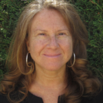 A woman with red shoulder-length hair and hoop earrings smiles at the camera