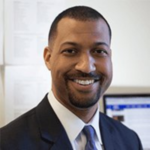 A man with short hair wearing a suit smiles at the camera