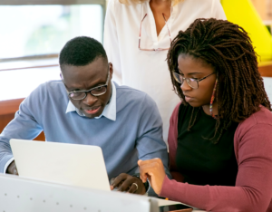 Two college-age students lean towards a laptop