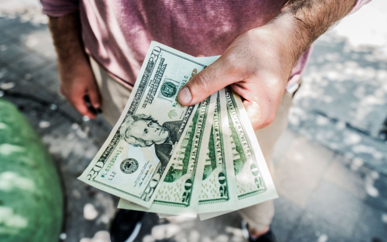 A person standing outside holds four $20 bills in one hand