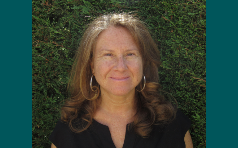 A headshot of a woman with red hair and silver earrings