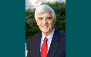 A man with short grey hair wearing a suit smiles