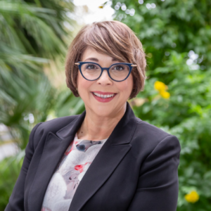 A woman wearing blue framed glasses and a black blazer