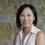 Woman with short black hair and wearing a white sleeveless blouse.